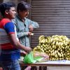 Street vendor selling bananas at an outdoor market with a customer purchasing fresh produce.