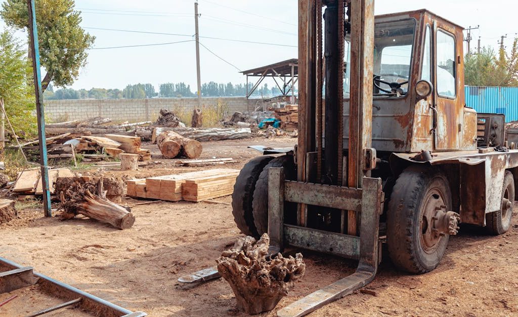 Old forklift in a rustic sawmill setting, surrounded by logs and lumber, hinting at heavy industry.
